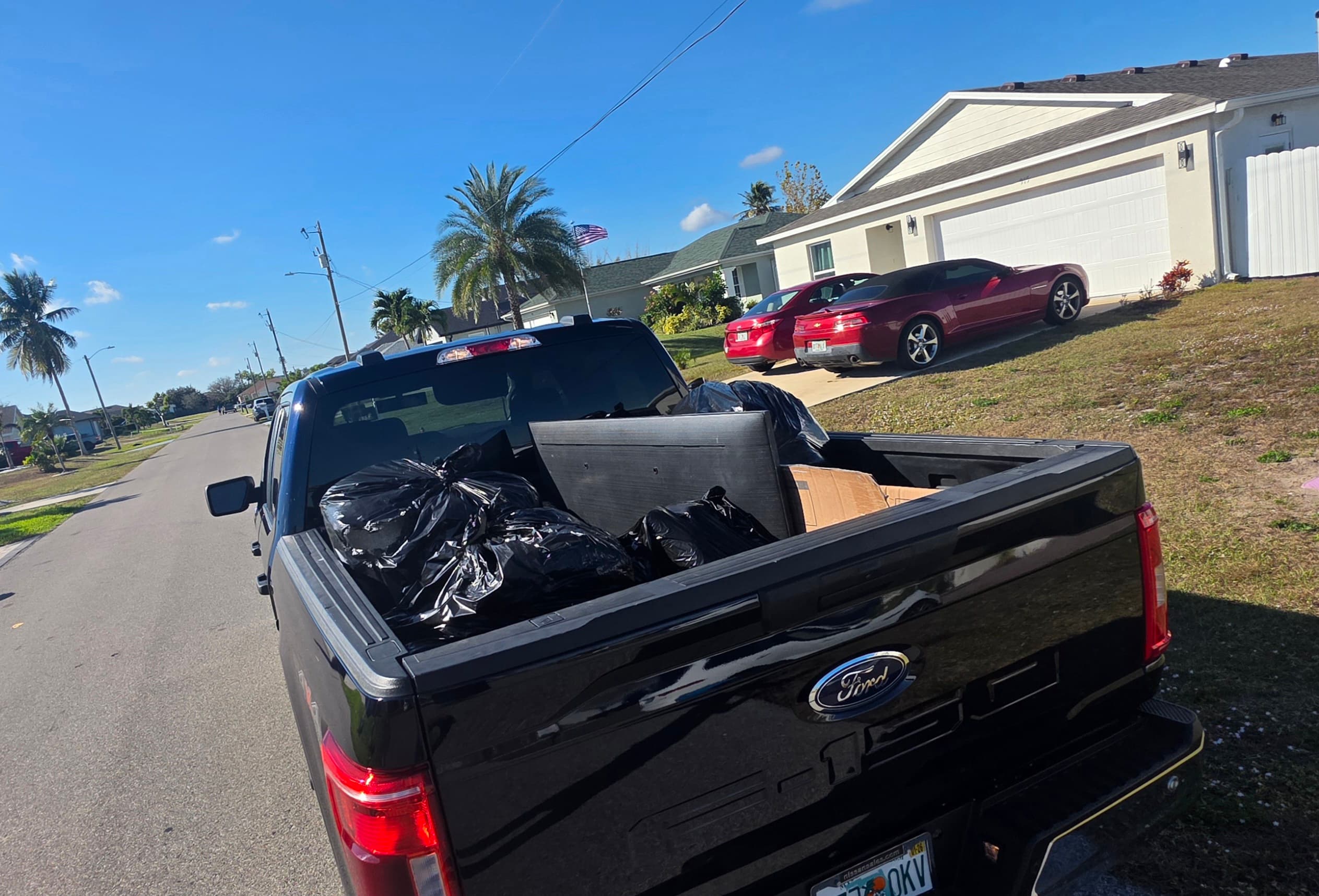Black Ford truck bed filled with trash bags and a television on a sunny street.