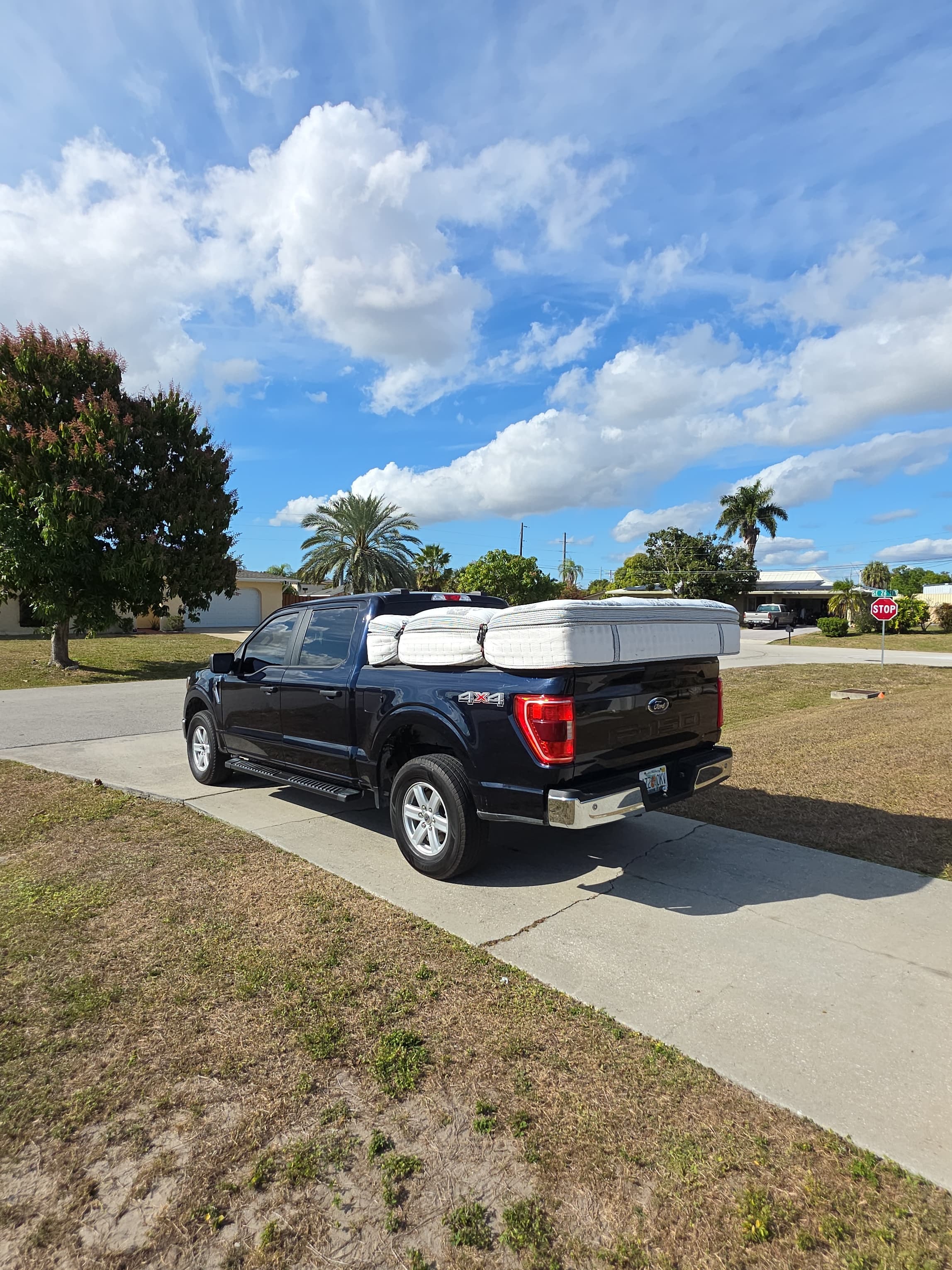 Black pickup truck with several mattresses stacked in the bed on a sunny driveway.